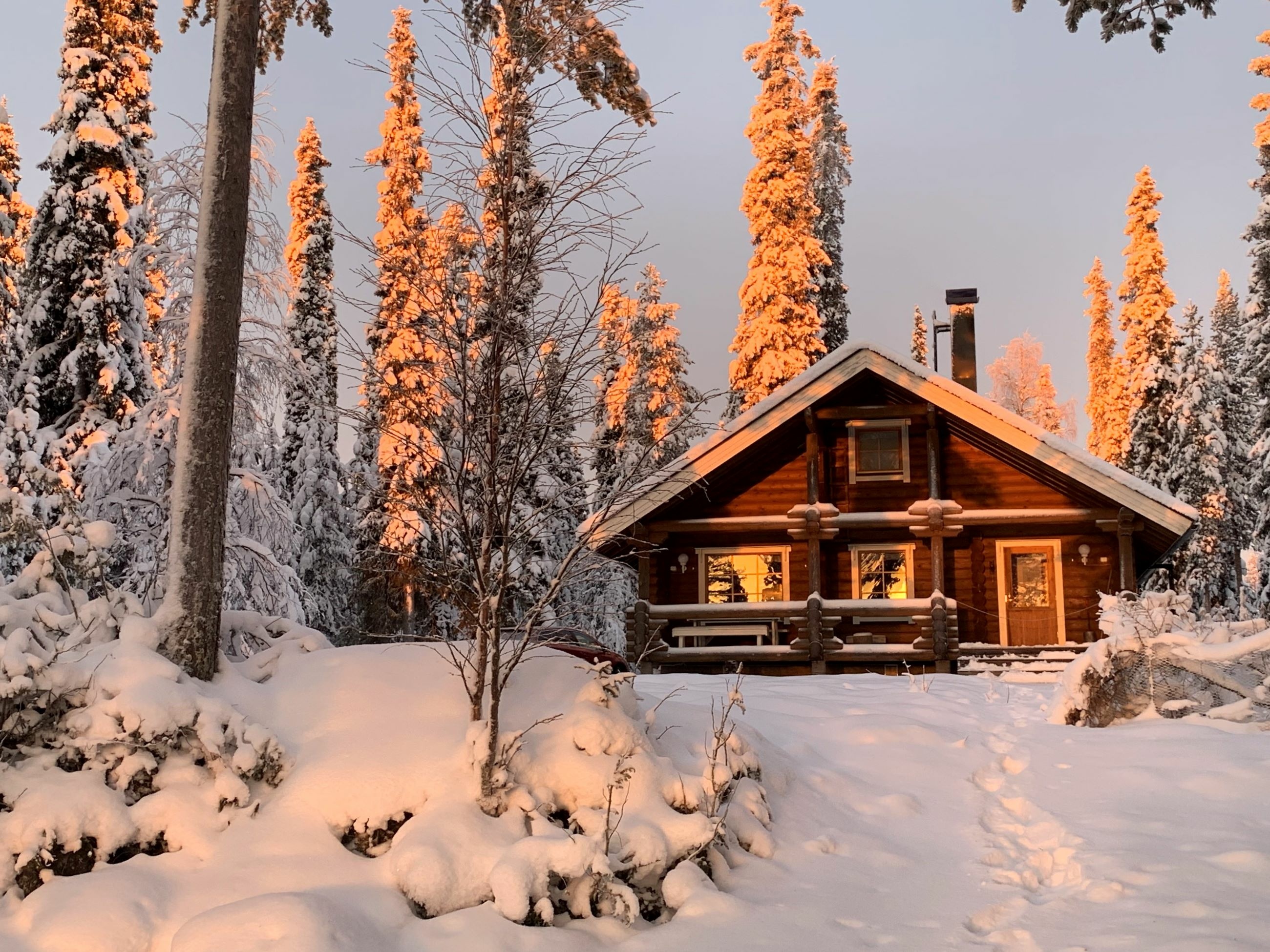 Cozy wooden log cabin sitting in a remote snowy forest during sunset